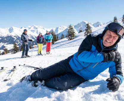 A male skier in winter gear lying on a snowy mountain slope clutching his shoulder in pain after a fall