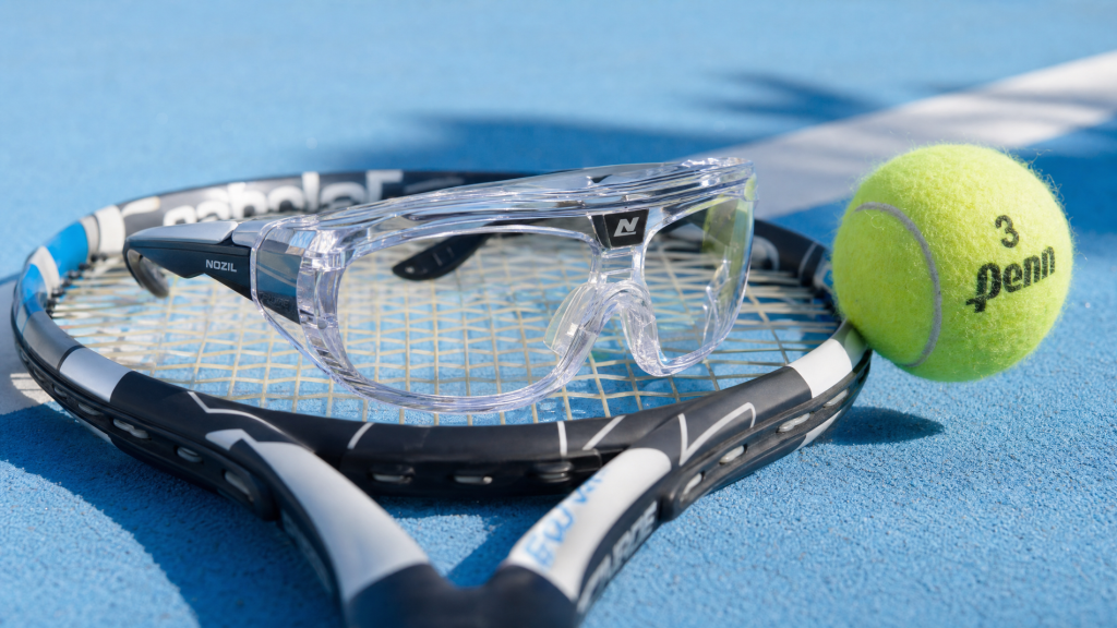 A close-up of professional protective sports goggles resting on a tennis racket on a court