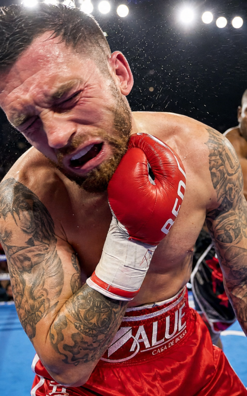A professional boxer in the ring clutching his jaw in pain after receiving a heavy punch during a match