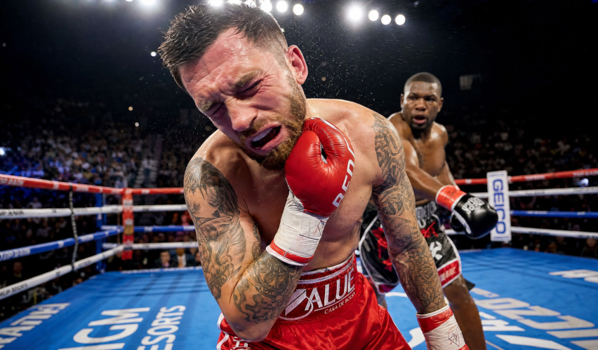 A professional boxer in the ring clutching his jaw in pain after receiving a heavy punch during a match