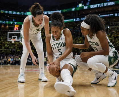 A female professional basketball player clutching her knee in pain on the hardwood court during a game