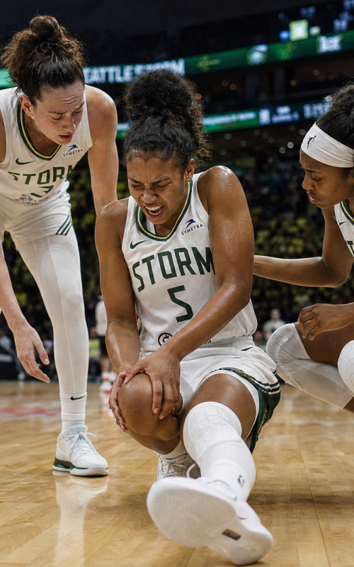 A female professional basketball player clutching her knee in pain on the hardwood court during a game