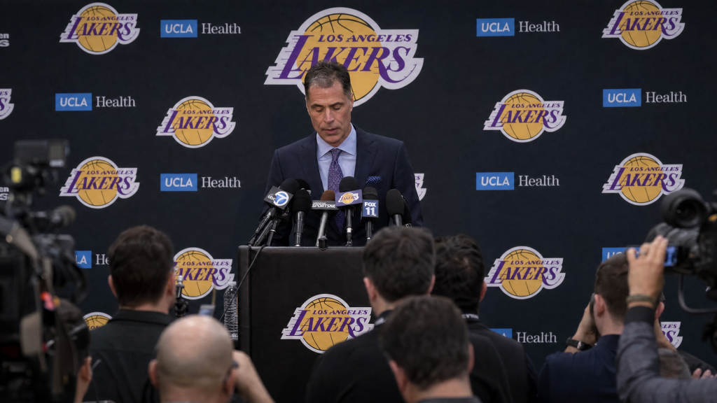 A sports team general manager speaking at a press conference podium announcing a player's season-ending injury