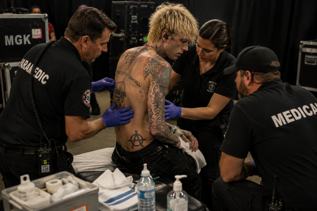 Medics examining MGK’s back injury backstage at concert